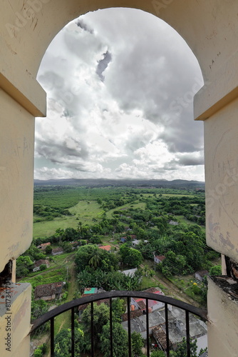 Land of the Manaca Iznaga Estate under cloudy sky framed by an arch of the Hacienda's belfry, Escambray mountains in background. Trinidad-Cuba-299 photo