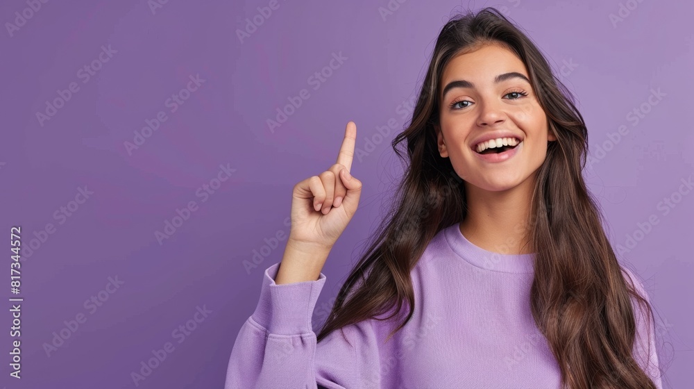 Portrait of beautiful young Hispanic or Latinx woman long hair wearing a purple sweatshirt smiling and pointing up on purple background, template for advertising or promotion, with copy space for text Portrait of beautiful young Hispanic or Latinx woman long hair wearing a purple sweatshirt smiling and pointing up on purple background, template for advertising or promotion, with copy space for text