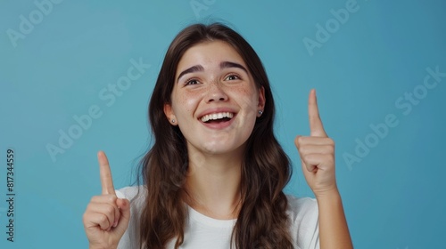 Portrait of beautiful young Hispanic or Latinx woman wearing a white t-shirt and pointing up with her fingers on a blue background  template for advertising or promotion  with copy space for text