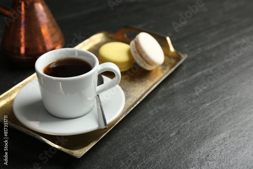 Tray with hot coffee in cup and macarons on dark textured table  closeup. Space for text
