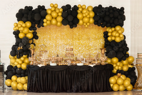 Photo zone for a table with candy bar sweets decorated with yellow gold and black balloons for a Halloween party in black and gold style