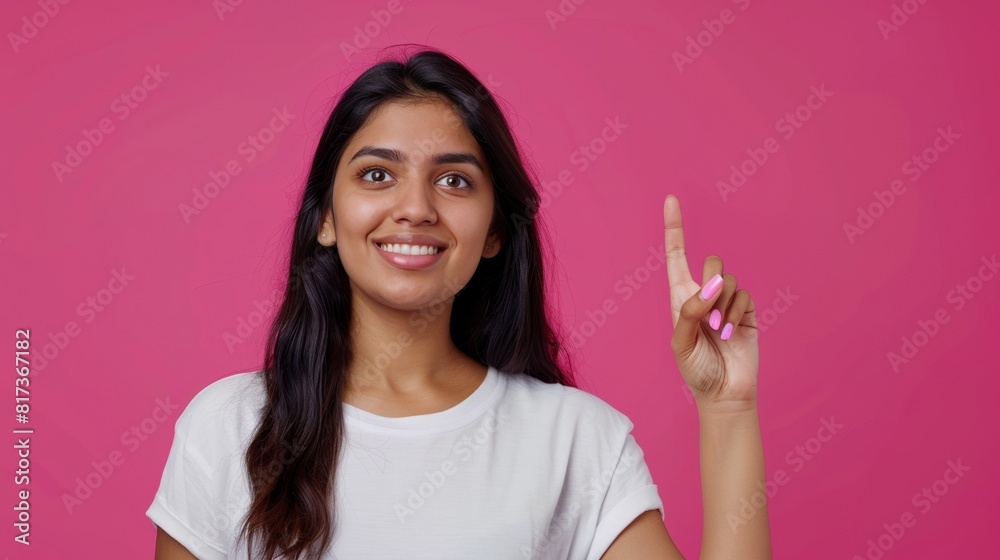 Portrait of beautiful young South Asian woman smiling wearing white t-shirt pointing up with one finger on a magenta background, template for advertising or promotion, with copy space for text Portrait of beautiful young South Asian woman smiling wearing white t-shirt pointing up with one finger on a magenta background, template for advertising or promotion, with copy space for text