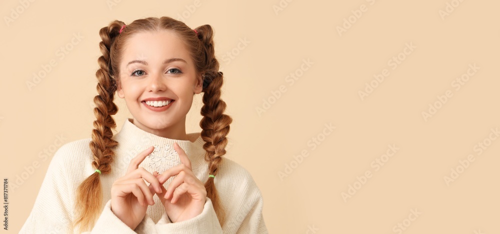 Happy beautiful young woman in warm sweater holding decorative snowflake on beige background with space for text