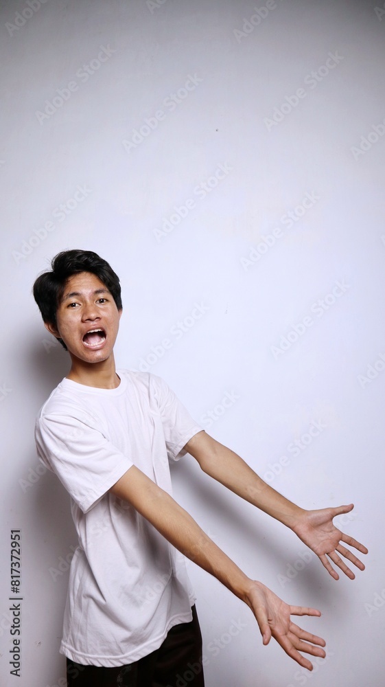 Excited young Asian man in white shirt with funny expression gesture pointing to the side Excited young Asian man in white shirt with funny expression gesture pointing to the side