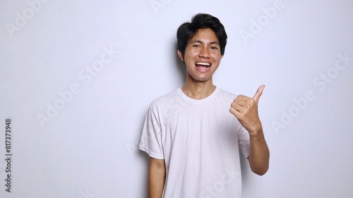 excited young asian man in white shirt with funny expression showing thumbs up okay, great, cool, steady, winning photo
