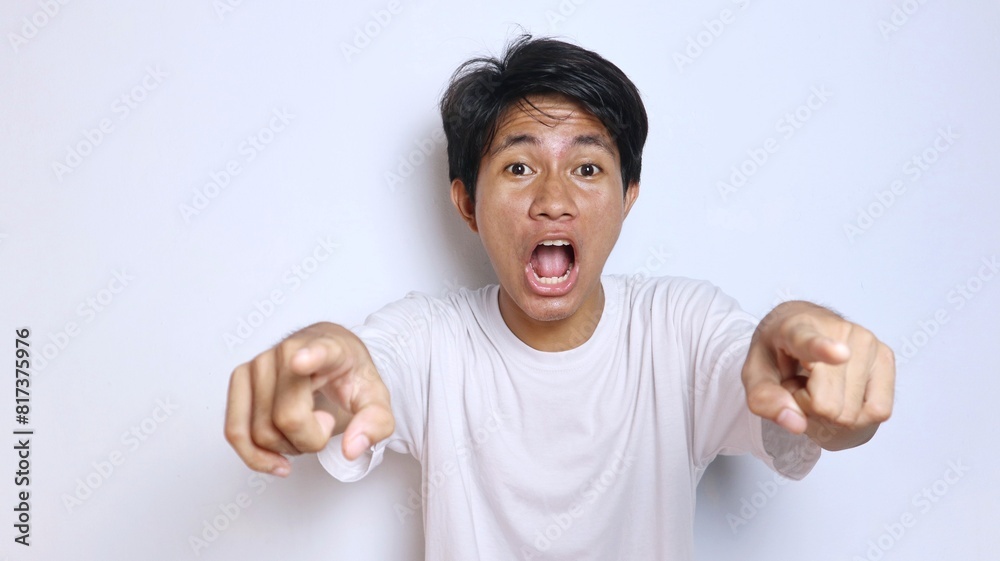 young asian man in white shirt with funny expression shocked gesture pointing forward, looking at camera young asian man in white shirt with funny expression shocked gesture pointing forward, looking at camera