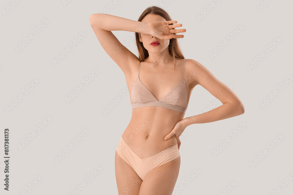 Beautiful young woman in stylish beige underwear on grey background