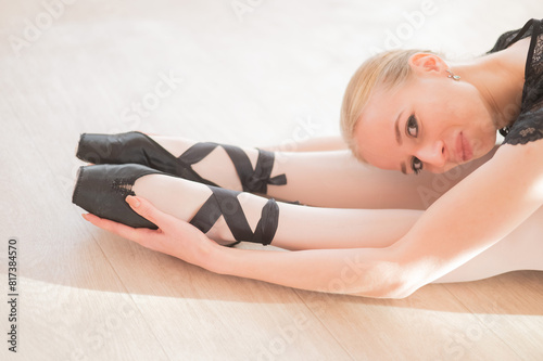 A young woman lies bent over on her feet in a ballet class. Ballerina stretches on the floor. 