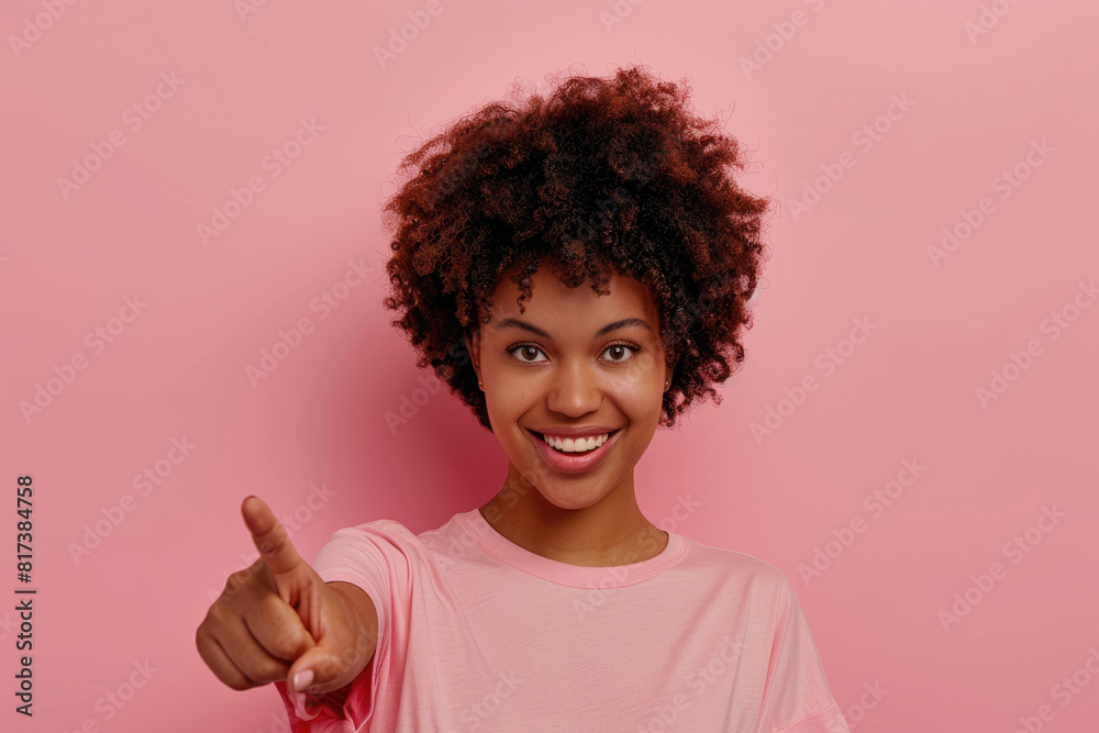 Photo of a happy black woman with afro hair wearing a casual t-shirt pointing his index finger at the camera on a pink background Photo of a happy black woman with afro hair wearing a casual t-shirt pointing his index finger at the camera on a pink background