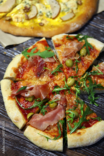 Pizzas with jamon, arugula, pear and cheese on a wooden surface.