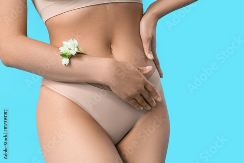 Beautiful young woman in panties with flowers on blue background, closeup photo