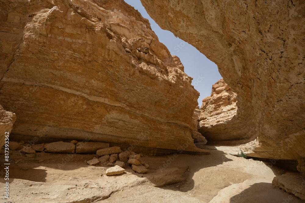 Narrow winding path cutting through heart of Tamaghza canyon, flanked by tall layered rock walls under hot Tunisian sun