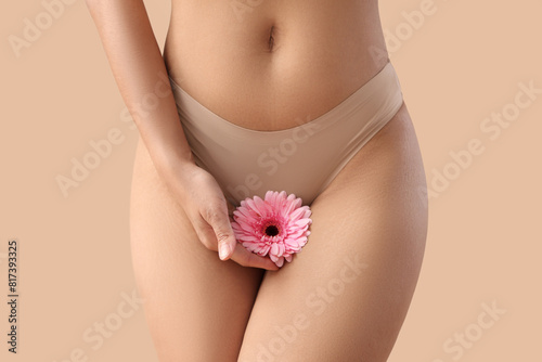 Beautiful young woman in panties with gerbera flower on beige background, closeup © Pixel-Shot