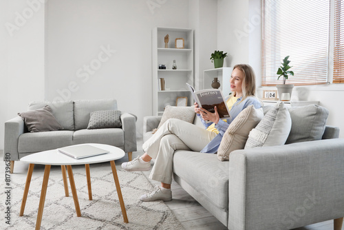 Young woman reading magazine on sofa in light living room