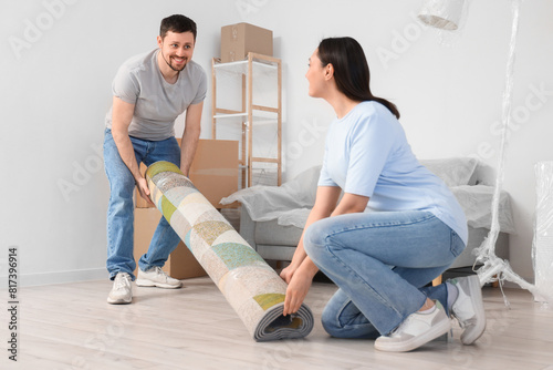 Young couple carrying rolled carpet in room on moving day photo