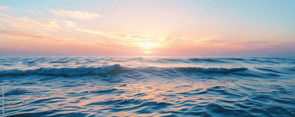 Calm ocean waves at sunset with a clear sky above. The serene water reflects the soft pastel hues of the setting sun, creating a peaceful and tranquil seascape.