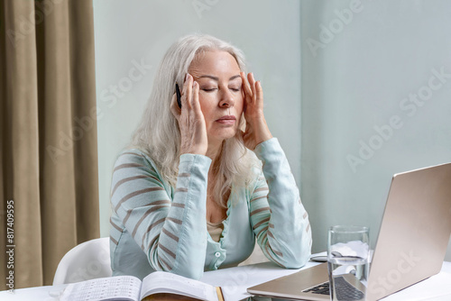 An elderly woman suffers from fatigue and headaches from working at the computer for a long time. photo