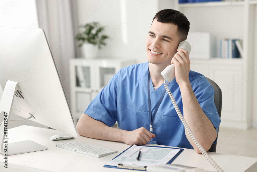 Smiling medical assistant talking by phone in office Smiling medical assistant talking by phone in office