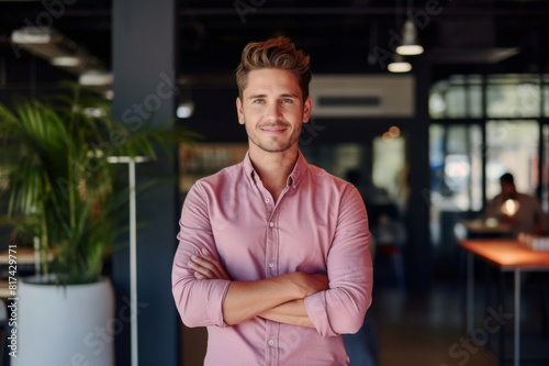 Portrait of smiling male professional with arms crossed in office. Confident businessman is standing at creative workplace. He is wearing shirt