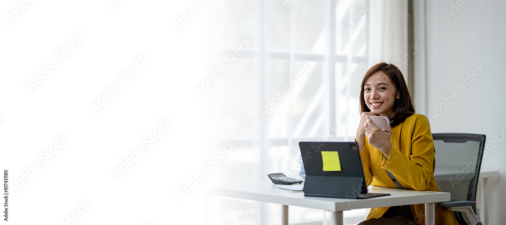 A woman is sitting at a desk with a laptop and a cup of coffee