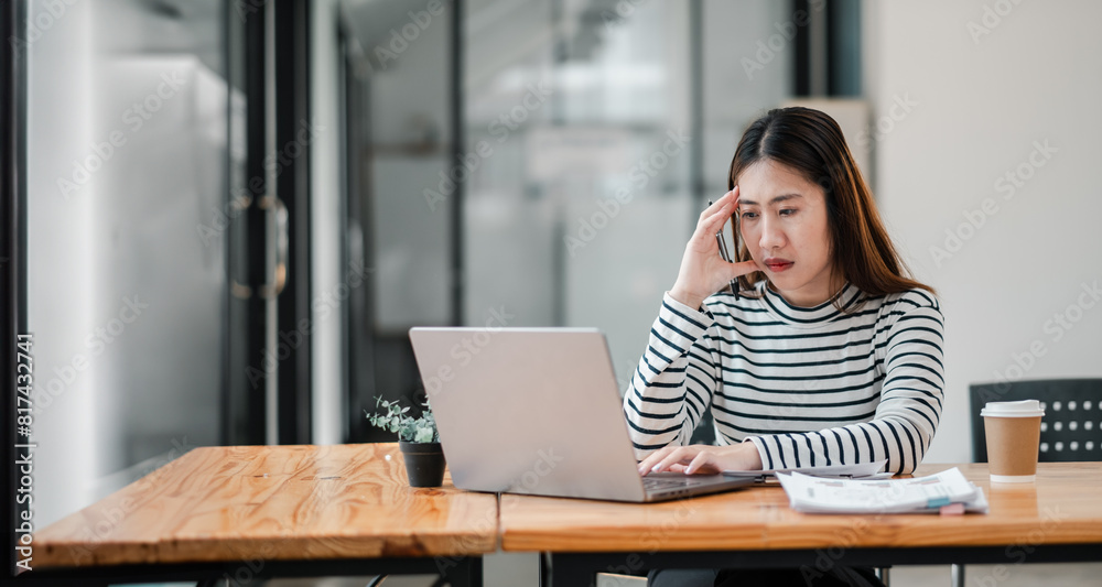 A woman is sitting at a desk with a laptop and a cup of coffee. She is talking on the phone and she is in a state of distress A woman is sitting at a desk with a laptop and a cup of coffee. She is talking on the phone and she is in a state of distress