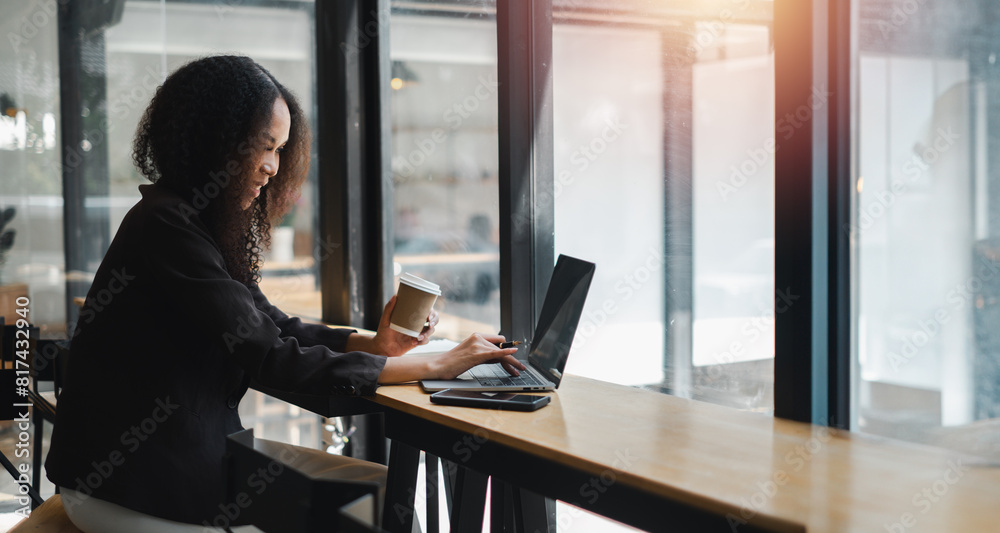 A woman is sitting at a table with a laptop and a cup of coffee. She is focused on her work and she is in a serious mood A woman is sitting at a table with a laptop and a cup of coffee. She is focused on her work and she is in a serious mood