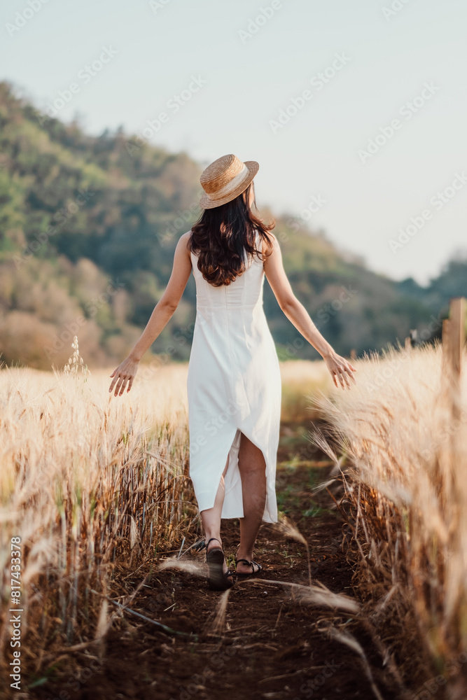 A woman wearing a straw hat walks through a field of tall grass. She is enjoying the outdoors and the peacefulness of the scene A woman wearing a straw hat walks through a field of tall grass. She is enjoying the outdoors and the peacefulness of the scene