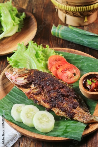 Mangrove Jack Grilled or Kakap Merah Bakar with indonesian spices served on tray and banana leaf and isolated Wodden background
 photo