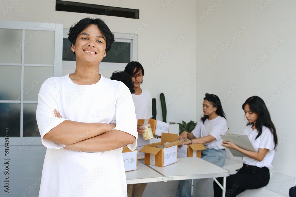Smiling Young Asian Man With Other Community Members Packing Food for Charity Event on The Background Smiling Young Asian Man With Other Community Members Packing Food for Charity Event on The Background