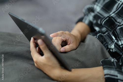 Closeup hand of young man using digital tablet while sitting on couch at home