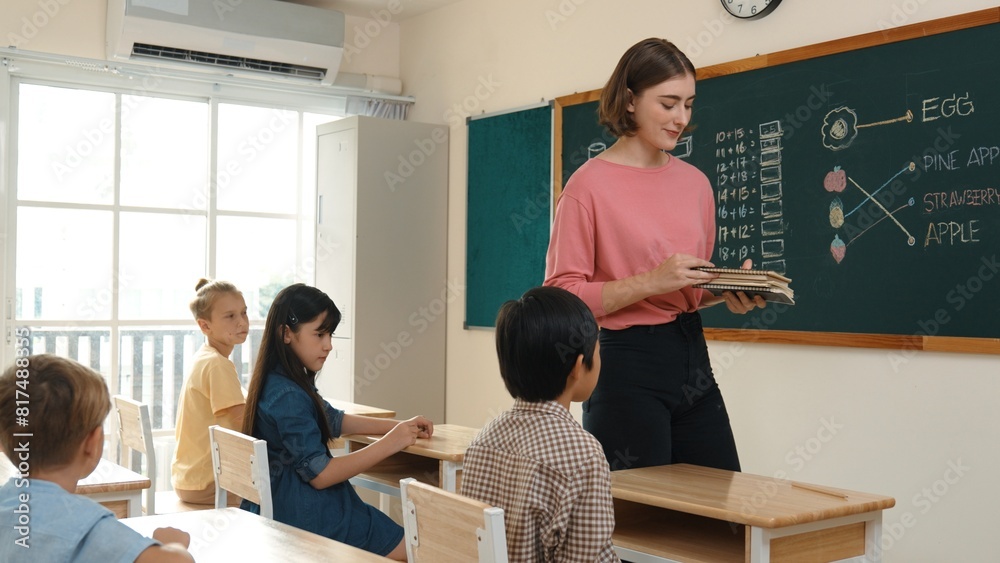 Instructor With Notebook Smart teacher checking cute student homework while explaining idea at ...