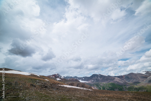 Harsh mountainous terrain with large sharp rocky ridge and range. High rock mountains with snow under gray cloudy sky. Rocks and stones on high mountain pass with stony hill. Big wide mountain wall.