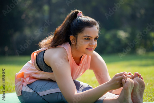 A Beautiful Blonde Woman While Sitting in the Park, Doing Yoga, and Trying to Touching Her Feet With Both Hands.
