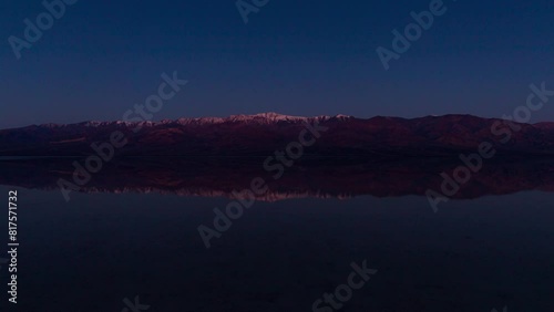 Timelapse wide shot of morning sun illuminating Panamint Range reflected in ancient Lake Manly at Badwater Basin in Death Valley National Park in California, USA photo