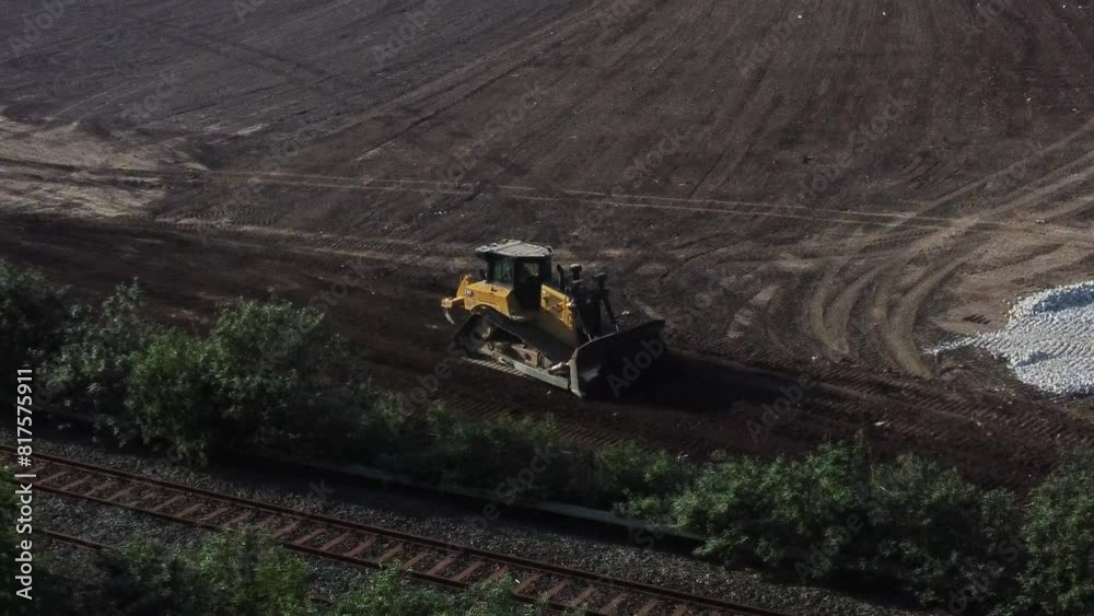 Bulldozer moving earth creating foundation road alongside railroad aerial dolly view on early morning sunrise construction site Bulldozer moving earth creating foundation road alongside railroad aerial dolly view on early morning sunrise construction site