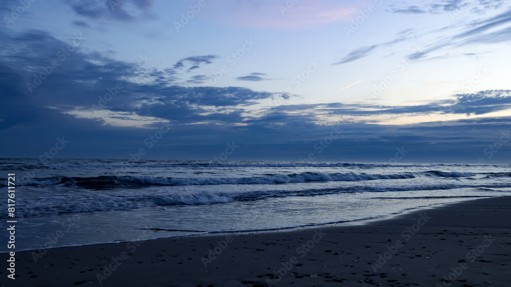 Dusk or dawn at a sandy beach; after sunset on a calm sandy beach in summer; before sunrise view over the sea with clouds and light blue sky
