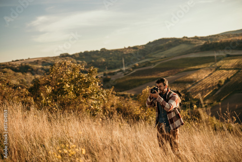 Outdoor enthusiast with a backpack exploring the golden hills, and photographing it with a camera