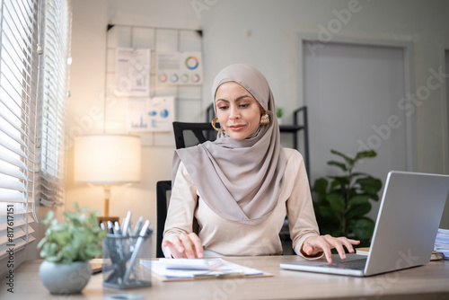 Young Muslim businesswoman wearing hijab sits working with laptop managing personal business in private office.
