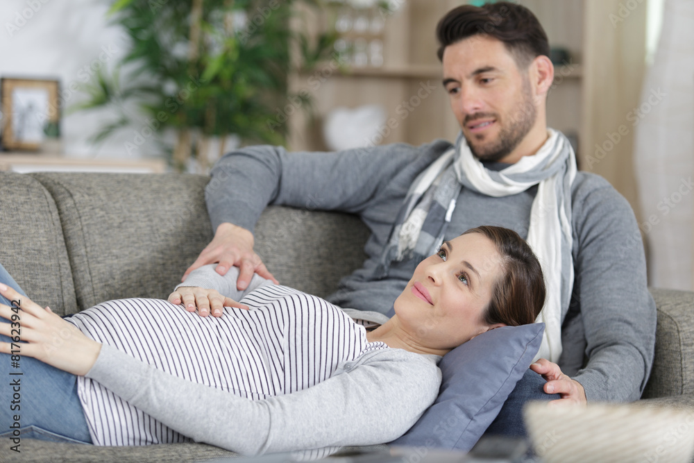 pregant woman and husband lying on couch toucher her belly pregant woman and husband lying on couch toucher her belly