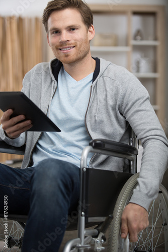 cheerful handsome wheelchaired blogger surfing the net while smiling photo