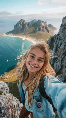 A woman is smiling and taking a selfie from the top of a mountain. The photo is taken from a high vantage point, giving a sense of adventure and excitement © vadosloginov