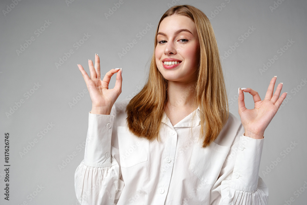 Young Woman Gesturing OK Sign With Hand Against a Neutral Background Young Woman Gesturing OK Sign With Hand Against a Neutral Background