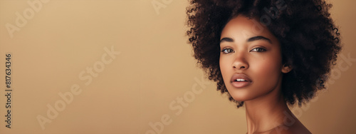 A woman with curly hair is standing in front of a tan wall. She has a serious expression on her face. Serene African American Beauty with Flawless Skin and Afro Curly Hair on a Beige Canvas