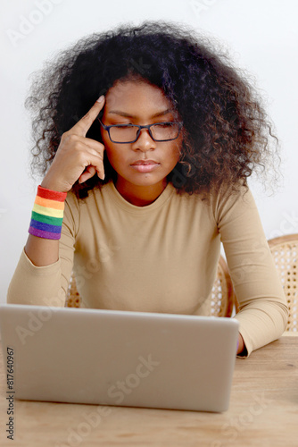 Stressed homosexual lesbian rainbow flag wristband using laptop computer to search pride celebration gift for surprise her girlfriend lover. African curly hair LGBT woman feeling anxious about gift.