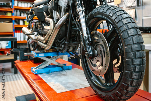 Close up of front wheel tyre and brake disk of custom motorbike on workshop. Front view of vintage scrambler motorcycle over platform ready to repair on cleaned mechanic garage.