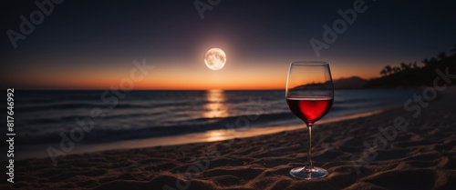 Glass of red wine on a sandy beach at night with full moon and copy space photo