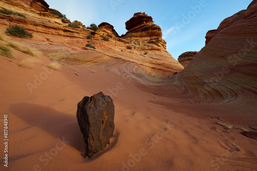 A lone rock in the sand in front of some wild rock formations in photo