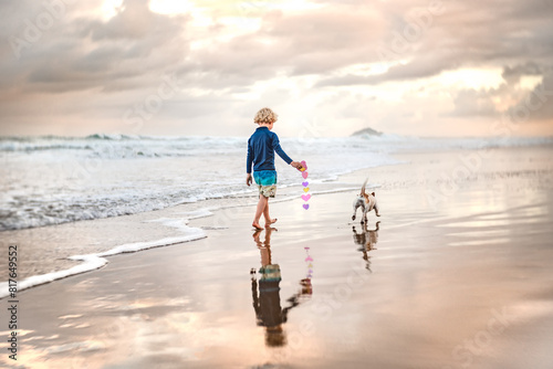 Child holding paper hearts walking on stunning beach with dog photo