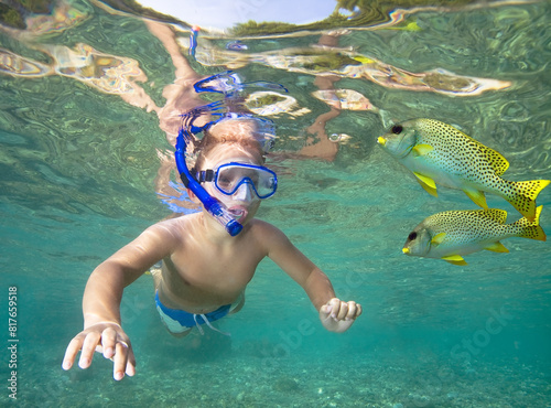 Little boy snorkeling with fishes in clear sea water.