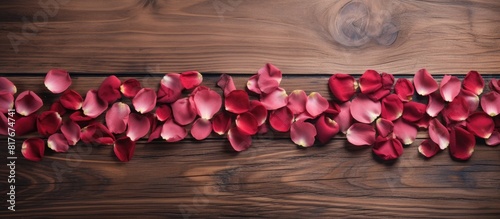 A love themed copy space image featuring red rose petals placed on a wooden background
